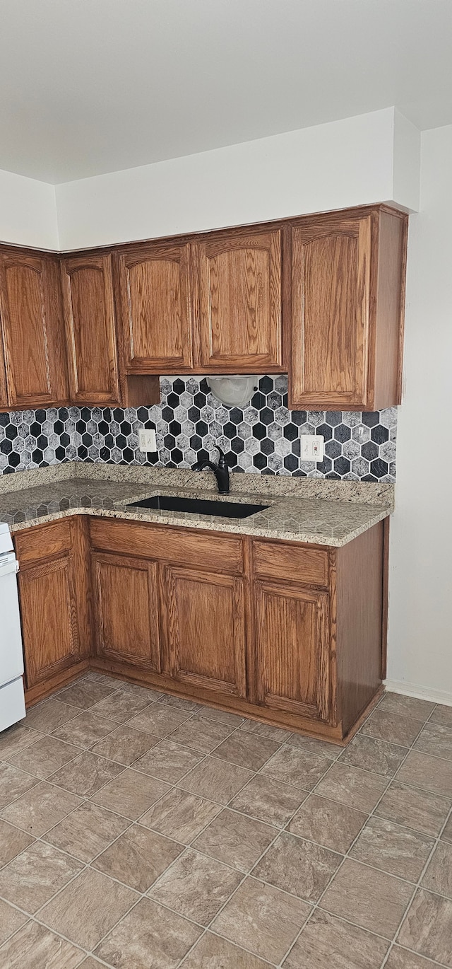 kitchen with tasteful backsplash, light stone counters, sink, and white stove