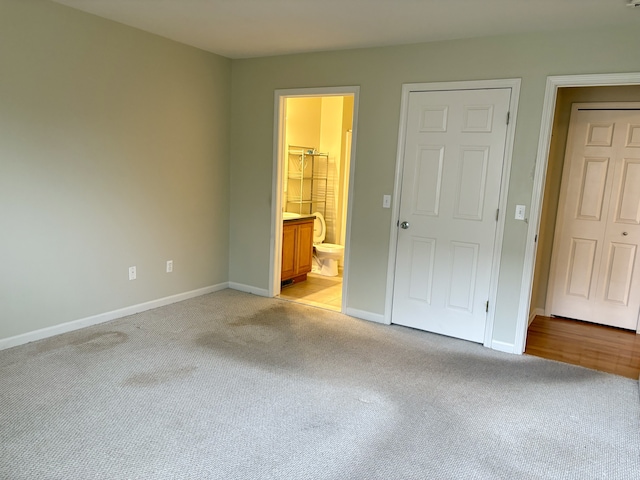 unfurnished bedroom with ensuite bathroom and light colored carpet