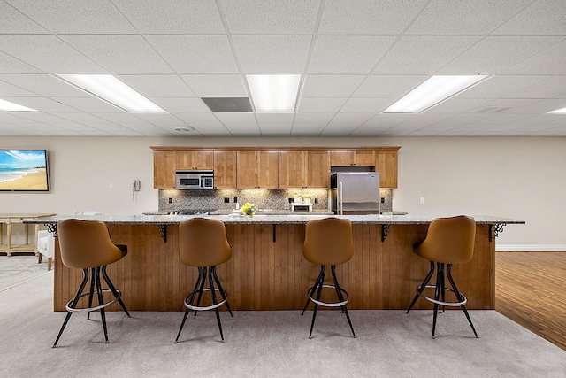 kitchen featuring appliances with stainless steel finishes, a paneled ceiling, tasteful backsplash, a breakfast bar area, and light colored carpet