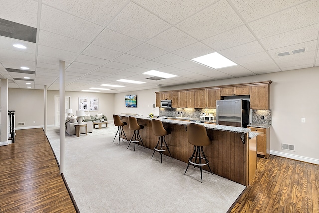 kitchen featuring a paneled ceiling, stainless steel refrigerator, tasteful backsplash, a breakfast bar area, and dark wood-type flooring