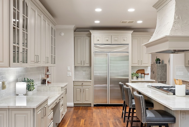 kitchen with backsplash, stainless steel appliances, light stone countertops, custom range hood, and a kitchen bar