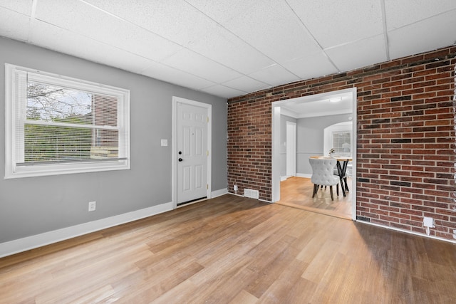 foyer entrance featuring hardwood / wood-style floors, a drop ceiling, and brick wall