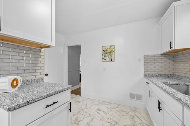 kitchen with white cabinets, tasteful backsplash, light stone countertops, and sink