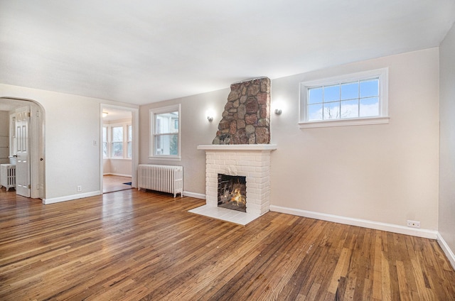 unfurnished living room with hardwood / wood-style flooring, plenty of natural light, a fireplace, and radiator