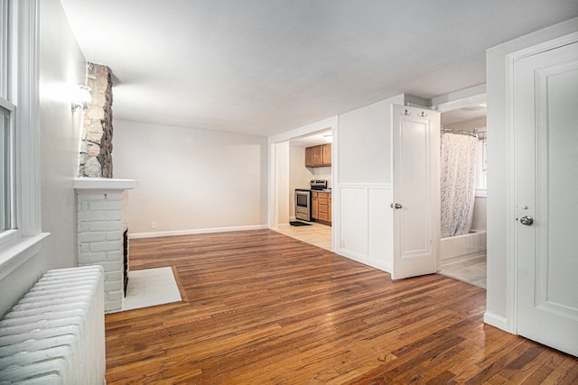 unfurnished living room featuring a brick fireplace, hardwood / wood-style flooring, and radiator heating unit