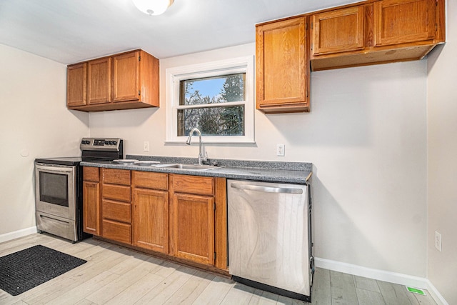 kitchen with appliances with stainless steel finishes, sink, and light wood-type flooring