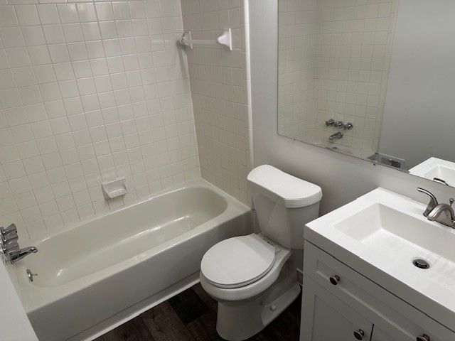 full bathroom with hardwood / wood-style flooring, vanity, tiled shower / bath combo, and toilet