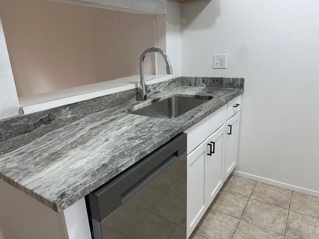 kitchen featuring dishwasher, dark stone counters, sink, light tile patterned floors, and white cabinetry