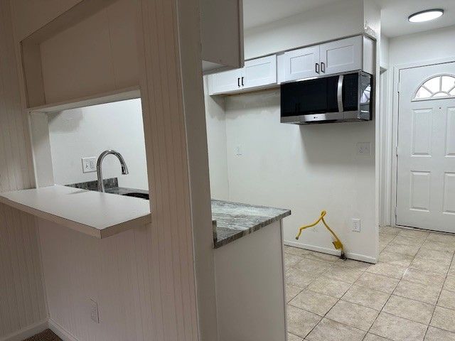 kitchen with sink, light stone countertops, light tile patterned floors, white cabinetry, and kitchen peninsula