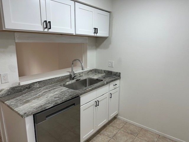 kitchen with white cabinets, light tile patterned floors, stainless steel dishwasher, and sink