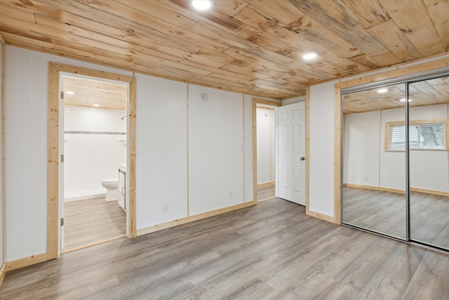 unfurnished bedroom with light wood-type flooring, a closet, wooden ceiling, and connected bathroom