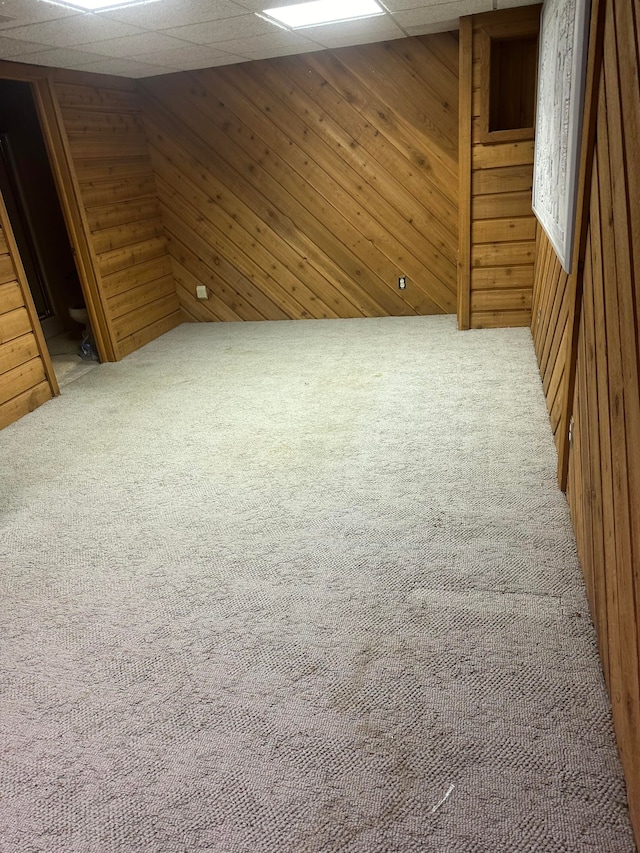 basement featuring a paneled ceiling, wood walls, and carpet