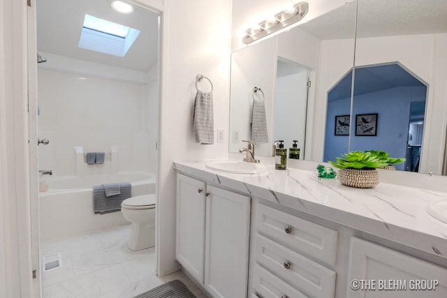 full bathroom with vaulted ceiling with skylight, vanity, a textured ceiling,  shower combination, and toilet