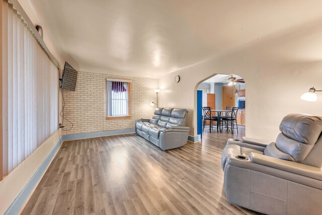 living room with hardwood / wood-style floors, ceiling fan, and brick wall
