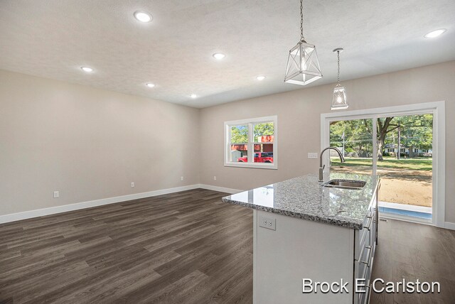 kitchen with a kitchen island with sink, dark wood-type flooring, hanging light fixtures, sink, and plenty of natural light