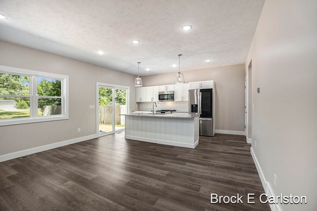 kitchen with dark wood-type flooring, a center island with sink, decorative light fixtures, white cabinetry, and stainless steel appliances