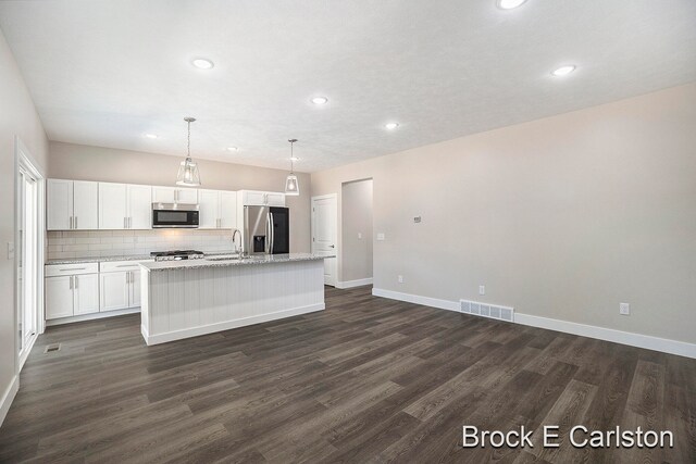 kitchen with hanging light fixtures, dark wood-type flooring, an island with sink, white cabinets, and appliances with stainless steel finishes