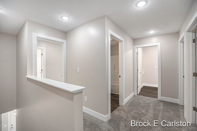 hall with dark colored carpet and a textured ceiling