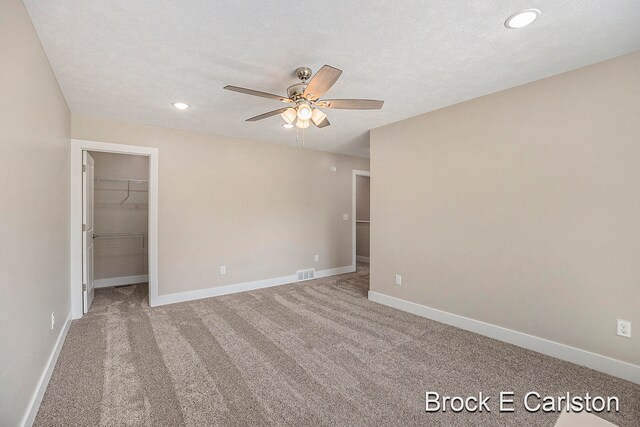 unfurnished bedroom with carpet, a walk in closet, a textured ceiling, ceiling fan, and a closet