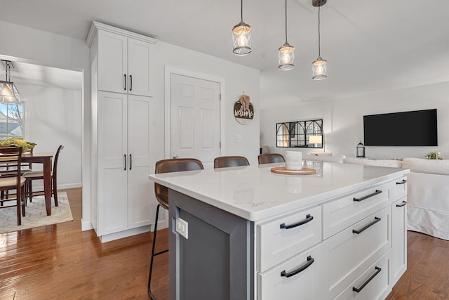 kitchen featuring pendant lighting, a center island, a kitchen breakfast bar, dark hardwood / wood-style floors, and white cabinetry