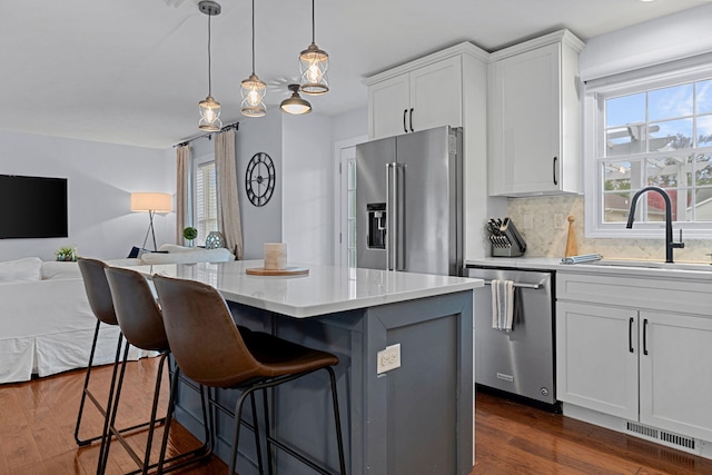 kitchen with a kitchen island, dark hardwood / wood-style flooring, decorative light fixtures, white cabinets, and appliances with stainless steel finishes