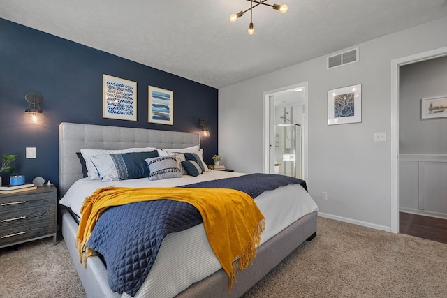 carpeted bedroom with ensuite bathroom, a chandelier, and a textured ceiling