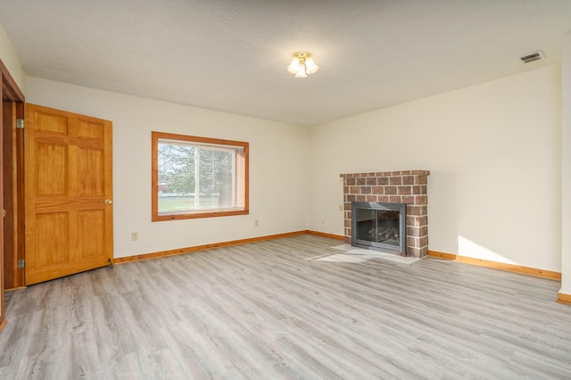 unfurnished living room with light wood-type flooring, a textured ceiling, and a brick fireplace