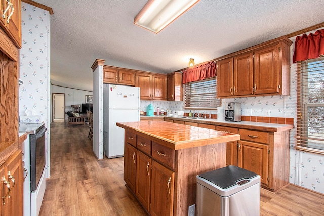 kitchen featuring light hardwood / wood-style flooring, a center island, white fridge, black / electric stove, and lofted ceiling