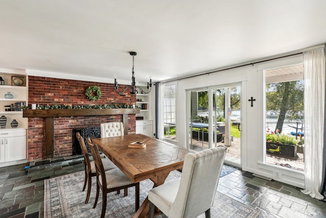 dining space featuring built in features, an inviting chandelier, a brick fireplace, and plenty of natural light