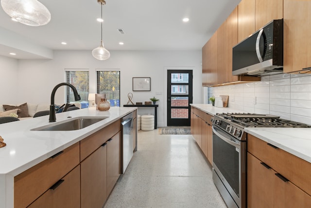 kitchen with light stone counters, sink, decorative light fixtures, and appliances with stainless steel finishes