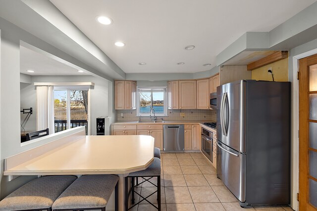 kitchen with a breakfast bar area, light countertops, appliances with stainless steel finishes, light brown cabinets, and a sink