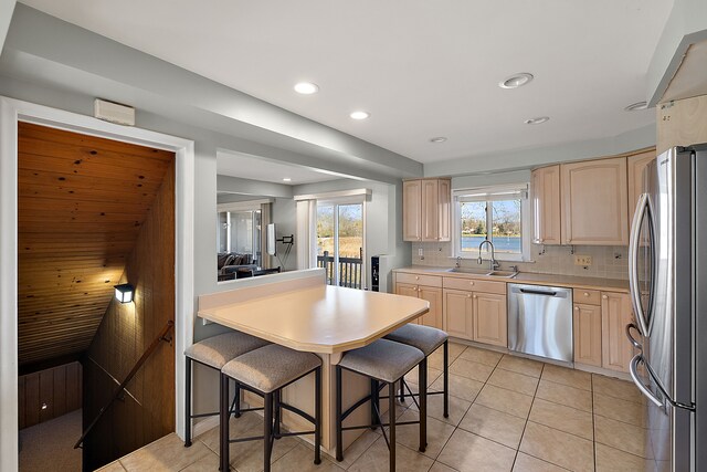 kitchen with sink, light brown cabinets, backsplash, a kitchen bar, and appliances with stainless steel finishes