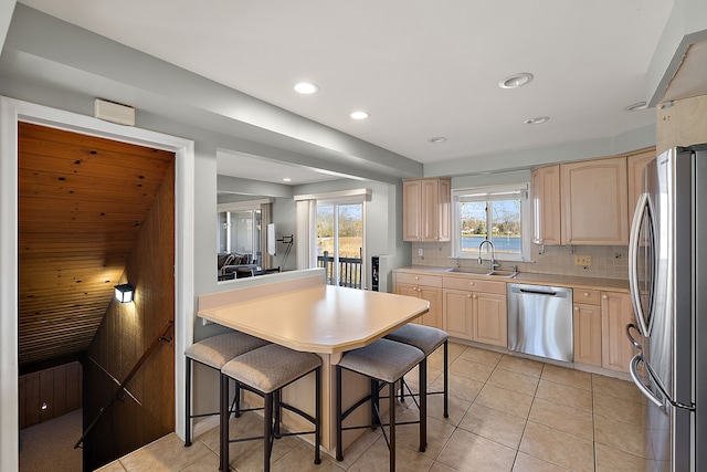 kitchen with light brown cabinetry, light countertops, a sink, stainless steel appliances, and backsplash