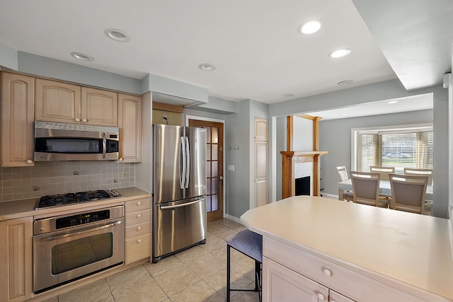 kitchen featuring light brown cabinetry, appliances with stainless steel finishes, light tile patterned flooring, light countertops, and decorative backsplash
