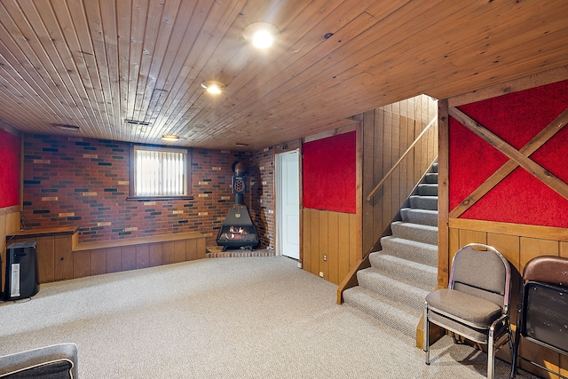 sitting room featuring wood ceiling, a wood stove, carpet flooring, brick wall, and stairs