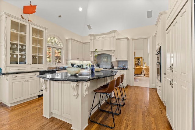 kitchen featuring a center island, lofted ceiling, white cabinets, a kitchen breakfast bar, and light hardwood / wood-style floors