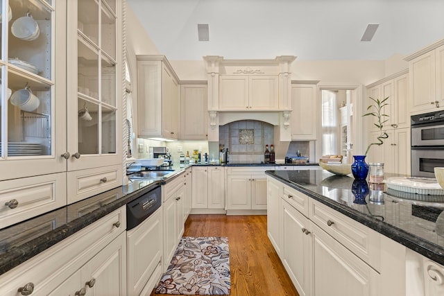 kitchen with tasteful backsplash, double oven, dark stone counters, dishwashing machine, and hardwood / wood-style flooring