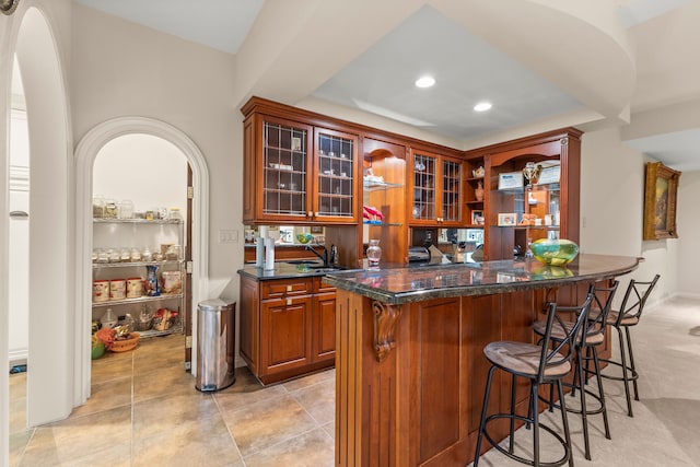 bar with dark stone countertops, light tile patterned floors, and sink