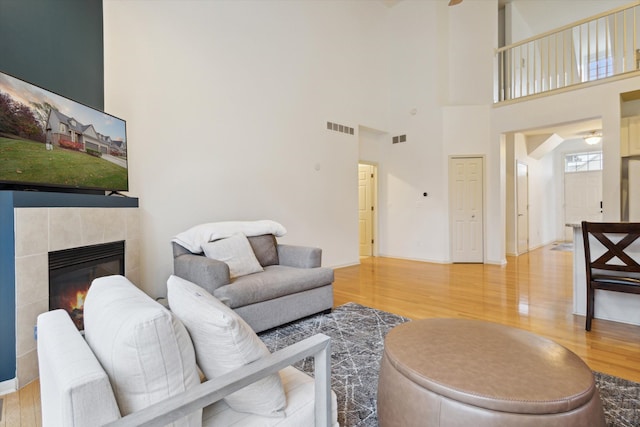 living room featuring a tile fireplace, visible vents, baseboards, and wood finished floors