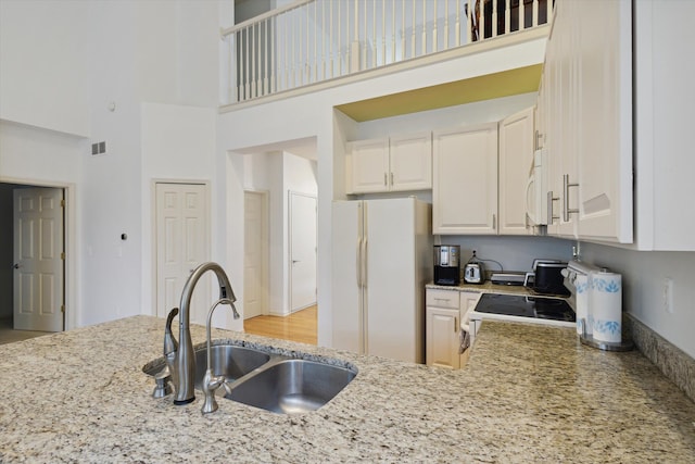 kitchen featuring light stone countertops, white appliances, a towering ceiling, and a sink