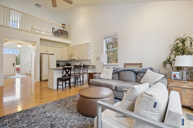 living area with high vaulted ceiling, a ceiling fan, and light wood-style floors