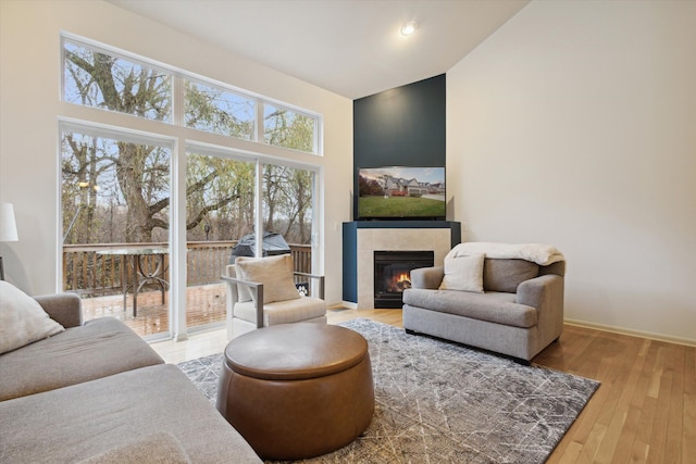 interior space with baseboards, a towering ceiling, a tiled fireplace, and wood finished floors