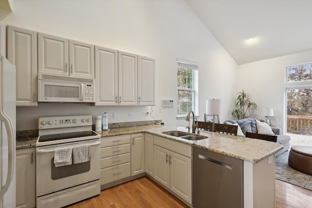 kitchen with white appliances, light wood-style flooring, open floor plan, a peninsula, and a sink