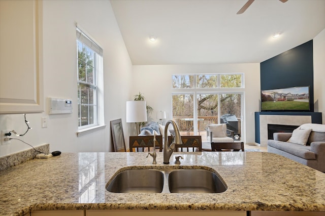 kitchen featuring light stone counters, a sink, a ceiling fan, open floor plan, and a tiled fireplace