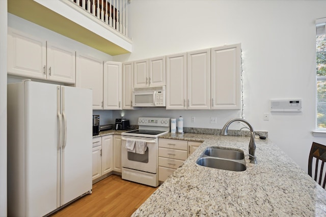 kitchen featuring light stone counters, white appliances, a sink, a towering ceiling, and light wood finished floors