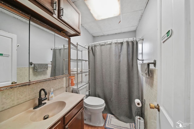 bathroom with a paneled ceiling, vanity, toilet, and backsplash