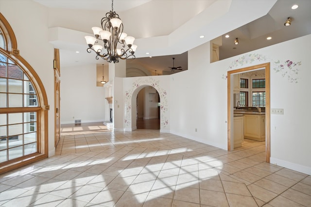 tiled empty room with ceiling fan with notable chandelier, a towering ceiling, sink, and a wealth of natural light