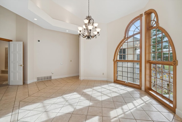 empty room featuring a towering ceiling, light tile patterned floors, a healthy amount of sunlight, and a notable chandelier