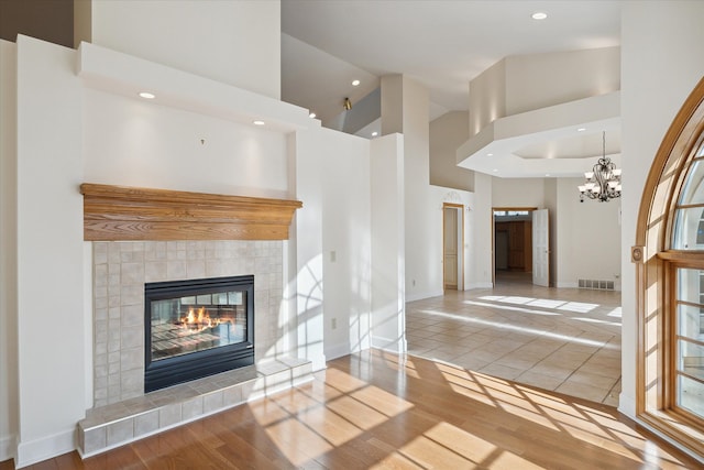 unfurnished living room featuring a tiled fireplace, hardwood / wood-style floors, high vaulted ceiling, and a chandelier