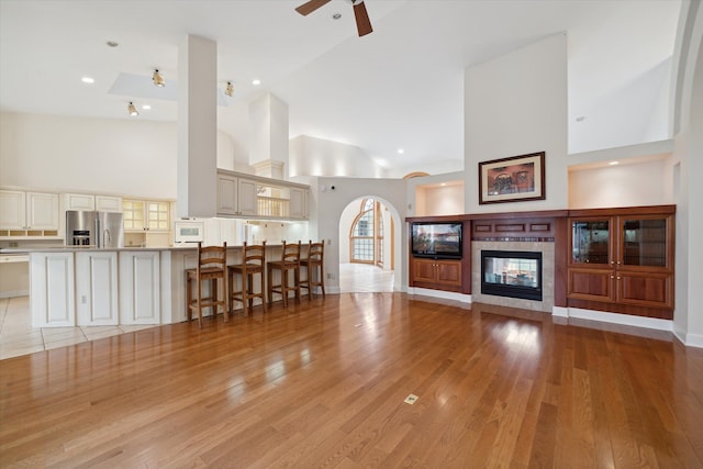 unfurnished living room featuring light wood-type flooring, high vaulted ceiling, ceiling fan, and a tiled fireplace